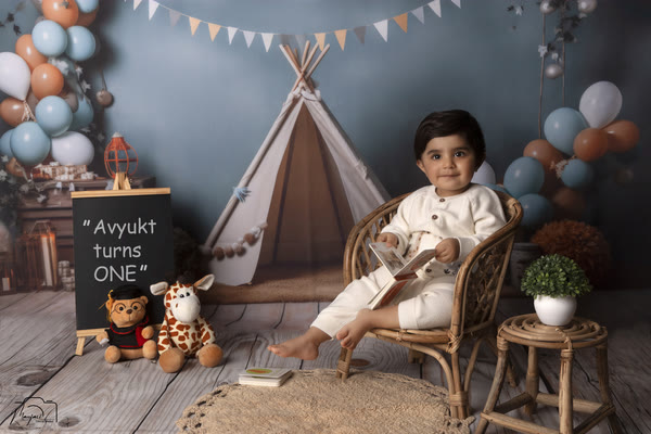 Toddler in a rattan chair at a first-birthday teepee set