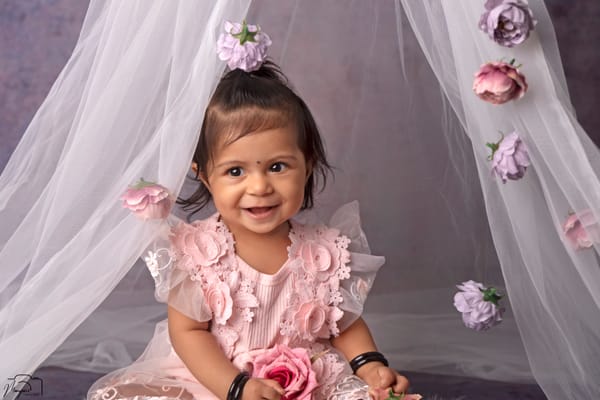 Smiling baby girl in a pink floral dress beneath a sheer canopy