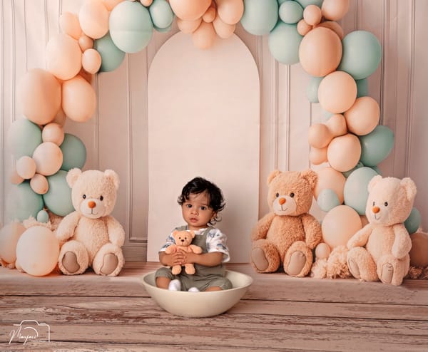 Baby in a white bowl among teddy bears beneath a peach and mint balloon arch