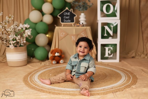 Smiling baby in a denim shirt at a green-balloon ONE birthday set
