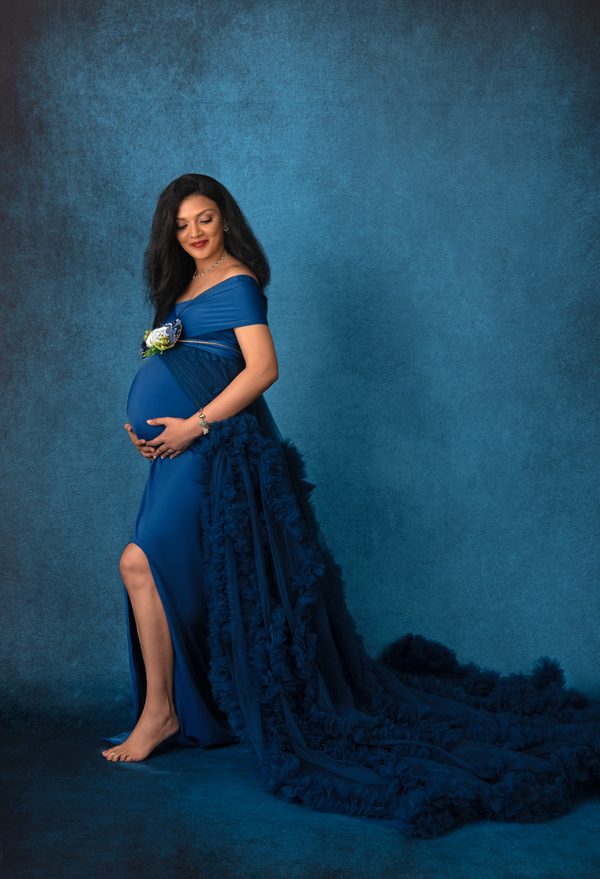 Expectant mother in a royal blue tulle gown against a deep blue backdrop