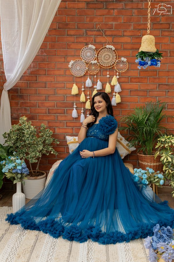 Expectant mother seated in a teal ruffled gown before a brick wall