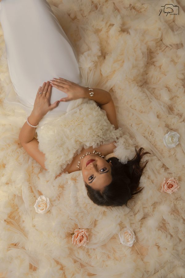 Expectant mother lying among cream feathers and roses
