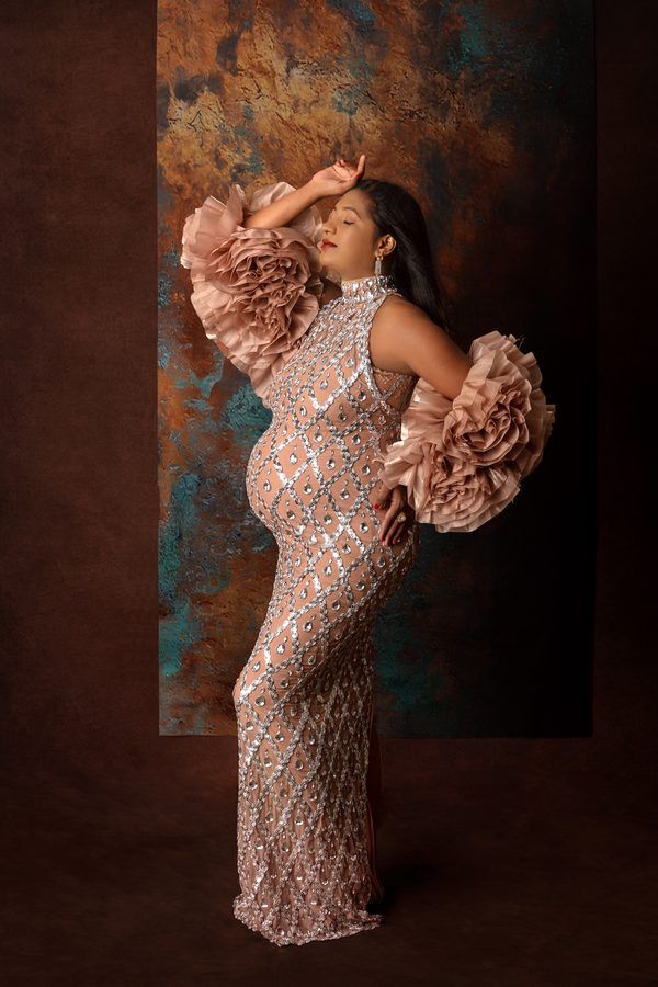 Maternity portrait in a sequinned gown against a textured copper backdrop