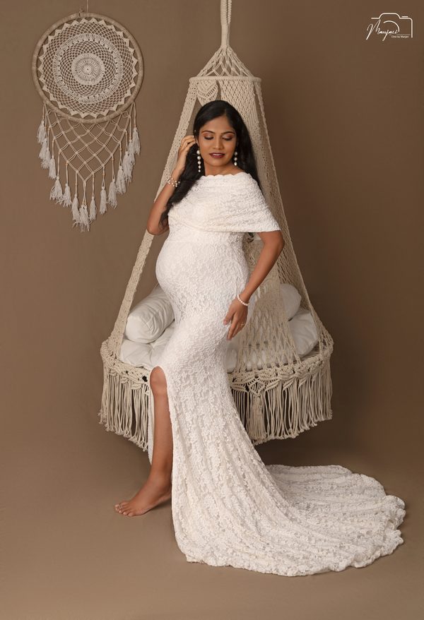 Expectant mother in white lace standing beside a macrame swing