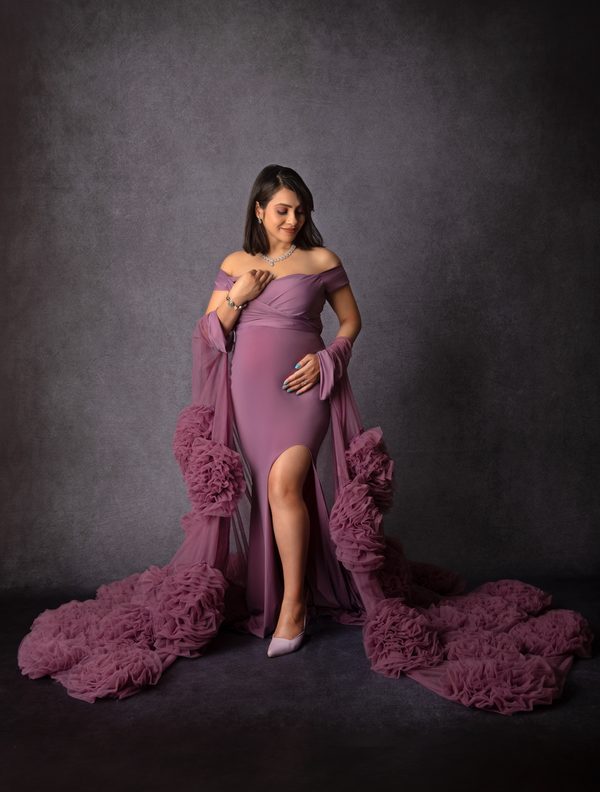 Expectant mother in a plum gown with a ruffled train on a dark set