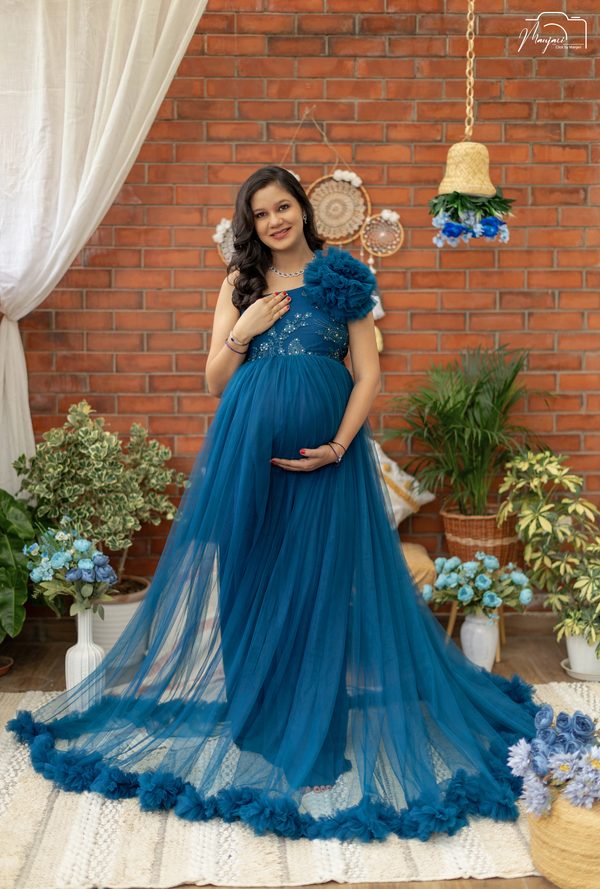 Expectant mother in a teal tulle gown before a brick wall with dreamcatchers