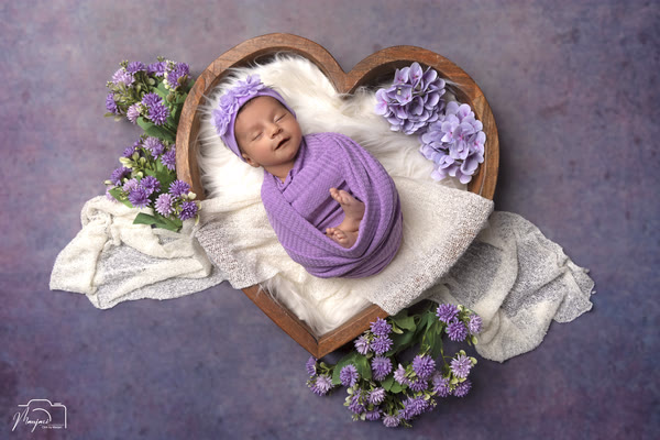 Sleeping newborn wrapped in lavender in a heart-shaped basket with purple flowers