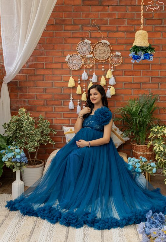 Expectant mother seated in a teal ruffled gown before a brick wall