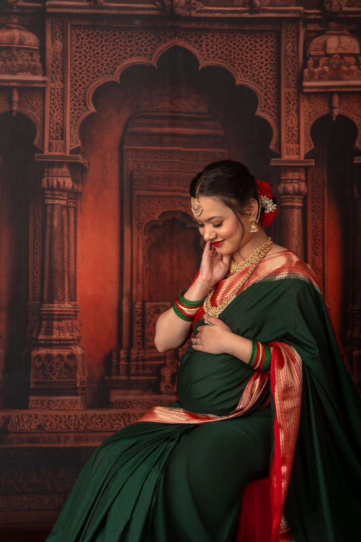 Maternity portrait in a green and red silk saree before a carved temple backdrop
